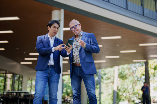 Businessmen collaborating, discussing information on smartphone outdoors