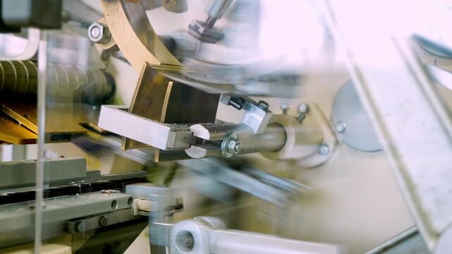 A close-up view of intricate machinery precisely wrapping chocolate candies in colorful paper packaging during factory production.