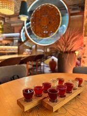 Assorted shot glasses with red and clear drinks served on wooden tasting boards