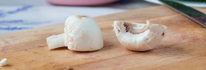 Two Champignons on a Chopping Block, Ready to Be Cooked - two mushrooms, one whole and one sliced, resting on a wooden cutting board