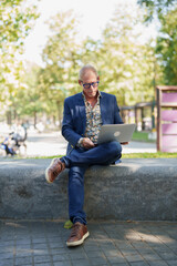 Obraz premium Senior man working outdoors on laptop in park