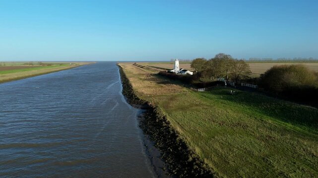 Drone video showing the white lighthouse guiding vessels from the Wash into the River Nene, surrounded by rural green landscapes in the UK.