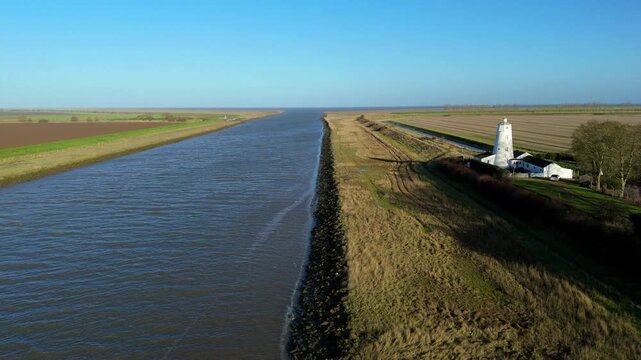Drone video showing the white lighthouse guiding vessels from the Wash into the River Nene, surrounded by rural green landscapes in the UK.
