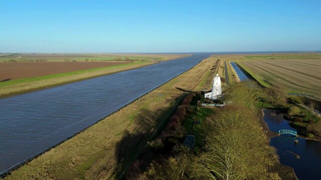 Drone video showing the white lighthouse guiding vessels from the Wash into the River Nene, surrounded by rural green landscapes in the UK.