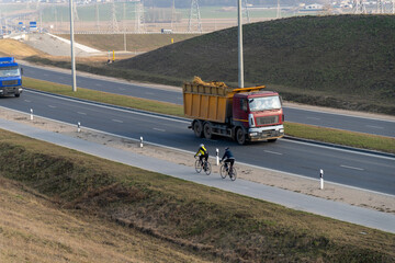 Two cyclists ride their bikes on a road parallel to a highway