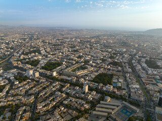 Naklejka premium Aerial view of the San Antonio neighborhood in Miraflores, Lima, showing the intersection of Benavides and La Merced avenues, surrounded by residential buildings and green areas at sunset.