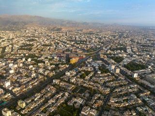 Aerial view of Ovalo Higuereta in Lima, Peru, connecting Surco and Miraflores districts, featuring the Metro train line, urban density, and mountains in the background during sunset.