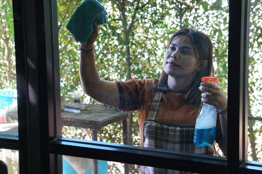 A close-up shot of a woman spraying cleaner and wiping the window, with focus on her expression and the cleaning activity.