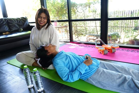 Two females relaxing after a yoga session, with a girl happily resting her head on the lap of the older woman. Two water bottles are placed on the green yoga mat. - Powered by Adobe