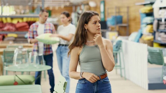 Girl look for something in room garden furniture store, searching for perfect item to complete patio. Young woman buyer looks around in showroom and chooses right furniture