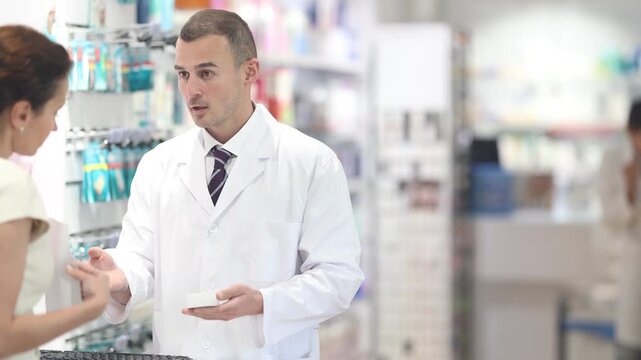 Polite male pharmacist consulting woman client about medicine indicated in her recipe in chemist's shop . High quality 4k footage