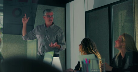 Male presenter pointing to chart on screen while team listens during modern office meeting with digital data visualization