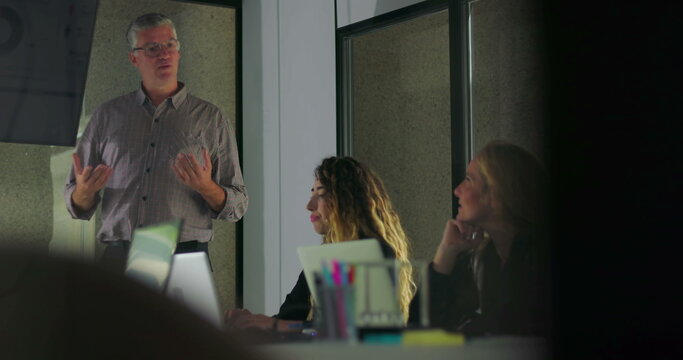Male professional presenting to group in conference room while female colleagues look on and engage with data charts on digital screen - Powered by Adobe