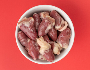 Raw Chicken Hearts in White Bowl on Vibrant Red Background