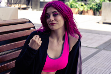 Confident young woman with magenta hair posing on bench