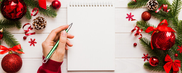 Woman writing Christmas to do list on notebook on colored background with xmas decorations