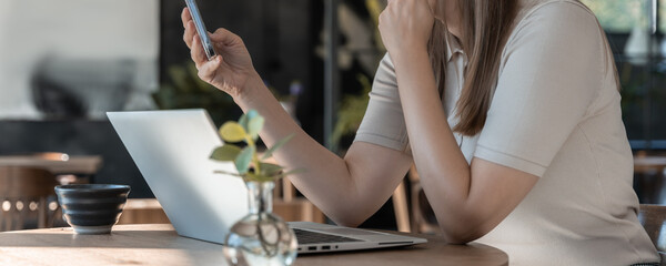 Obraz premium Woman Using Smartphone While Working On Laptop At Table In Bright Café Interior