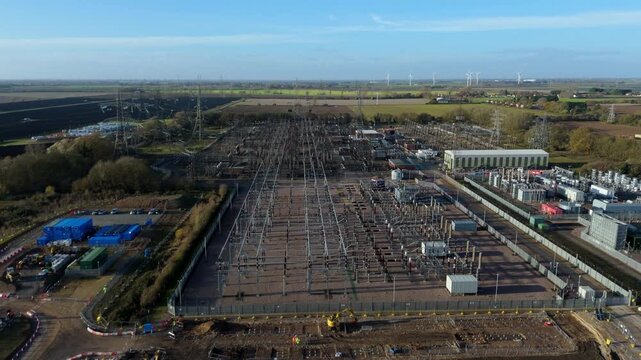 Aerial drone view of vast electrical substation with pylons, transformers, solar fields, wind turbines, and synchronous condensers in Walpole St Peter, UK