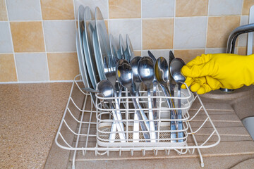  A hand with a yellow washing up glove on in the kitchen putting a clean spoon in a rack, chore concept