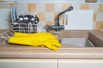A pair of yellow washing up gloves next to the kitchen sink after the washing up has been done