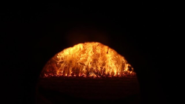 A powerful view of bright orange flames and embers inside an industrial furnace or boiler, framed by a dark arched opening.