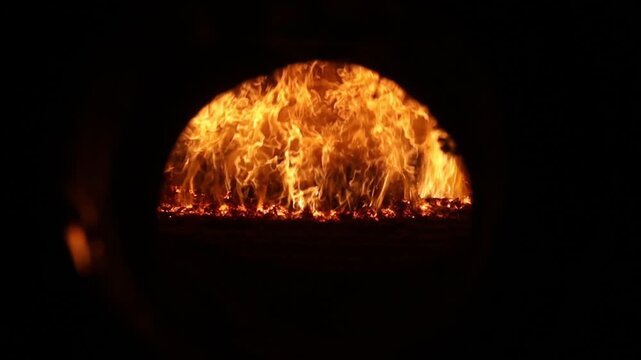 A powerful view of bright orange flames and embers inside an industrial furnace or boiler, framed by a dark arched opening.