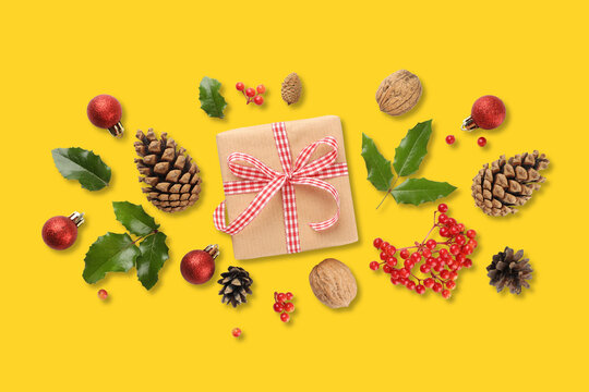 Gift wrapped with red ribbon among pinecones and holly leaves