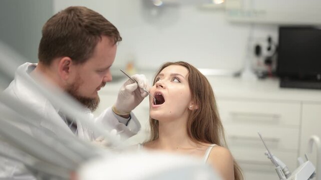 Male dentist delicately checks teeth of a young woman with the help of instruments. European woman came to the dentist office for a dental check and caries prevention. High quality 4k footage