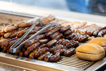 Nürnberger Rostbratwürste liegen in mehreren Reihen auf einem Grill an einem Verkaufsstand. 