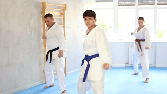 Three athletes have taken starting position and studying and repeating sequence of punches and painful techniques in karate kata technique. Oriental martial arts, training and obtaining black belt