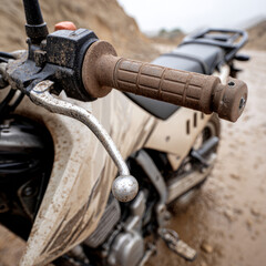 A dirt-covered motorcycle handlebar in a sandy terrain.
