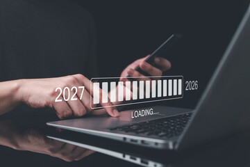 Close-up of hands using laptop and smart phone with futuristic holographic loading bar showing 2026 to 2027 transition, symbolizing progress, digital growth, innovation and future business planning.