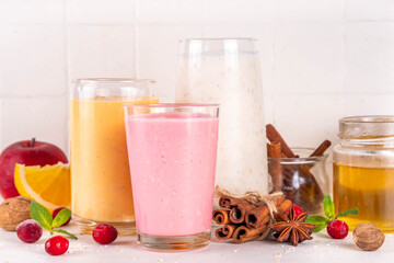 Autumn winter spicy fruit smoothie set. Various flavor tasty smoothie drinks in 3 glasses with yogurt, oats, seasonal fruits - apple, orange, cranberry, with anise and cinnamon