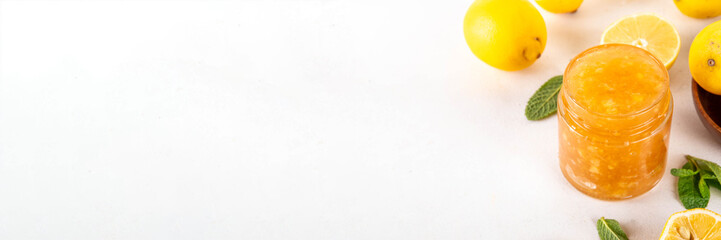 Sweet and sour lemon citrus jam marmalade preserves in small jar with fresh ginger, lemons and mint, on white table copy space