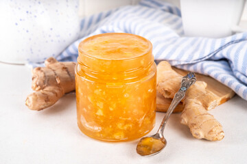 Homemade caramelized ginger jam marmalade preserves in small jar with fresh ginger roots on white table copy space