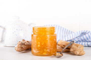 Homemade caramelized ginger jam marmalade preserves in small jar with fresh ginger roots on white table copy space