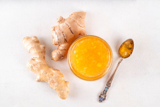 Homemade caramelized ginger jam marmalade preserves in small jar with fresh ginger roots on white table copy space