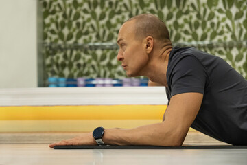 Holding sphinx pose caucasian man stretching spine and chest in indoor fitness studio focusing on...