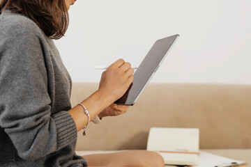 Woman sitting indoors and using a digital tablet with a stylus, working in a calm home environment.