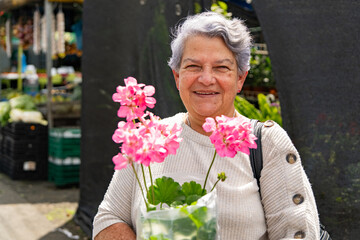 Fototapeta premium Smiling senior woman holding pink flowers at outdoor market