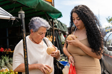 Hispanic women standing at tropical fruit stall sipping coconut water