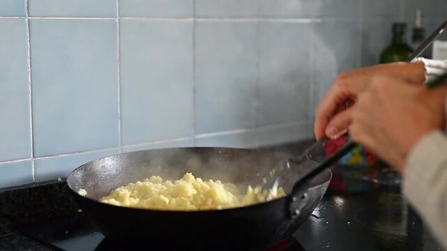 Cooking traditional Granada style flour migas in a full rustic pan with a woman&rsquo;s hands in a home kitchen