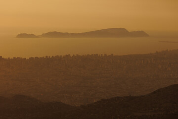 Obraz premium Hillside shantytown contrasting with a distant modern city skyline in the mist, illustrating social inequality, poverty, and urban sprawl in Lima, Peru