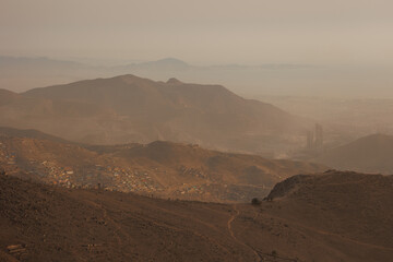 Hillside shantytown contrasting with a distant modern city skyline in the mist, illustrating social inequality, poverty, and urban sprawl in Lima, Peru