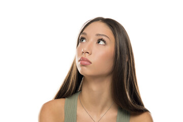 Studio shot of young woman with long brown hair wearing green tank top, looking up with thoughtful expression, on white background.