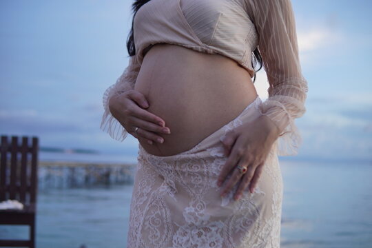 Close-up of a pregnant woman’s belly gently cradled by hands wearing rings.