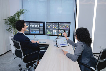 Business professionals analyzing data and discussing financial reports with digital dashboards and graphs in a modern office setting, focusing on strategy and performance.