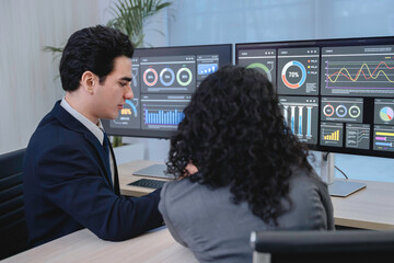 Business professionals analyzing data and discussing financial reports with digital dashboards and graphs in a modern office setting, focusing on strategy and performance.