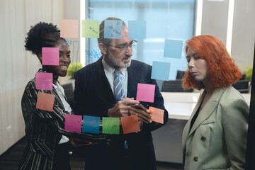 Diverse business team brainstorming ideas using sticky notes and digital tablet in modern office, teamwork and collaboration in creative planning session.