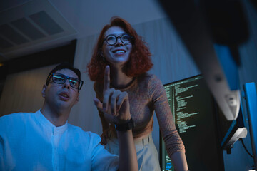 Two software developers collaborating at night, focusing on code review and debugging process on a computer screen, representing teamwork, innovation, and modern software development workflow.
